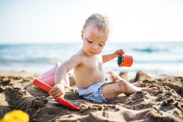 A small toddler girl sitting on beach on summer holiday, playing.