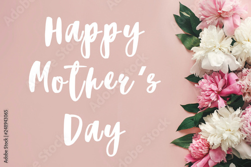 Happy Mother's Day text sign on peonies flat lay. Pink and white peonies border on pastel pink paper with space for text.  Stylish floral greeting card.