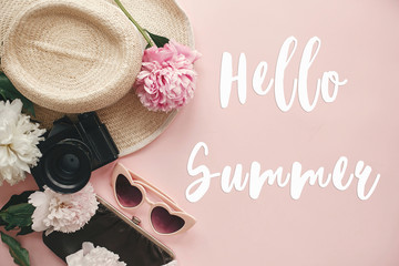 Obraz na płótnie Canvas Hello Summer text sign on stylish photo camera, retro sunglasses, hat, peonies on pastel pink paper. Summer vacation and travel concept, girly image