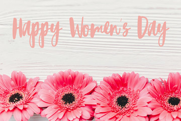 Happy Women's Day text sign at pink gerbera on white wooden background,  flat lay. Floral greeting card. Girl Power. International womens day, 8 march.