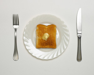 MELTING BUTTER ON SLICE OF TOAST ON WHITE PLATE WITH KNIFE AND FORK