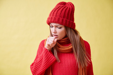 Ill girl in the red sweater standing on the yellow background, sore throat