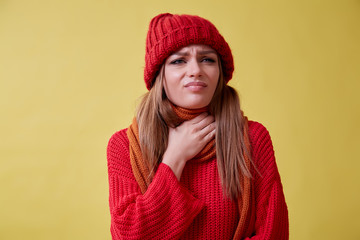 Ill girl in the red sweater standing on the yellow background, sore throat