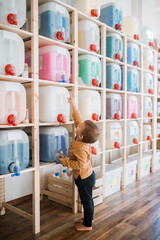A small toddler boy standing by dispensers in zero waste shop.