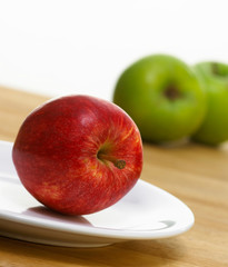 FRESH RED APPLE ON WHITE PLATE WITH GREEN APPLES IN BACKGROUND