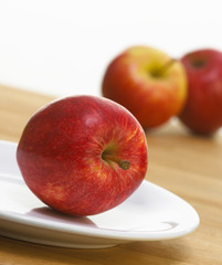 FRESH RED APPLE ON WHITE PLATE WITH RED APPLES IN BACKGROUND