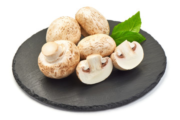 Champignons on a slate shale plate with basil, close-up, isolated on white background
