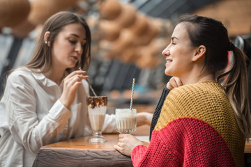 Two happy women are sitting in a cafe, drinking milkshakes,