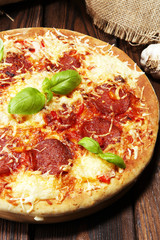 Italian pizza with salami, peperoni - with melted cheese, red tomatoes and green basil on a table decorated by cheese, tomato and cherry tomatoes