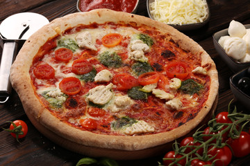 Pizza with tomatoes, mozzarella cheese, black olives and basil. Delicious italian pizza on wooden pizza board.