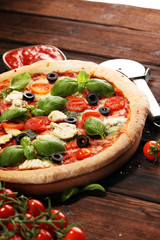 Pizza with tomatoes, mozzarella cheese, black olives and basil. Delicious italian pizza on wooden pizza board.
