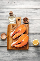 Raw salmon steaks with spices, herbs, salt and lemon on a wooden table background