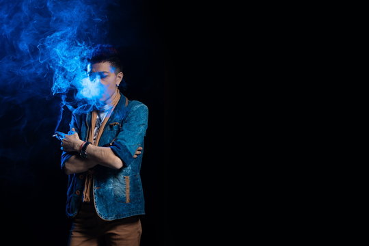 A woman with red hair in a denim suit smokes a cigarette and releases a bym in blue light on a black background