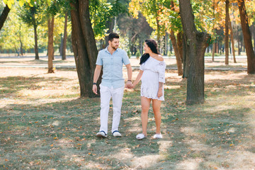 Pregnant girl walks in the park with her husband, hugging and kissing, enjoying the beautiful weather