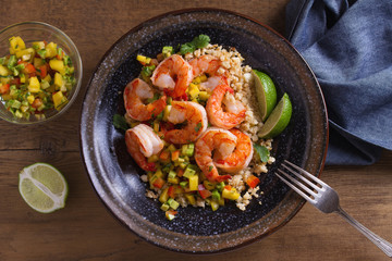 Shrimps with mango avocado and red pepper salsa on cauliflower rice in bowl on wooden table. View from above, top studio shot