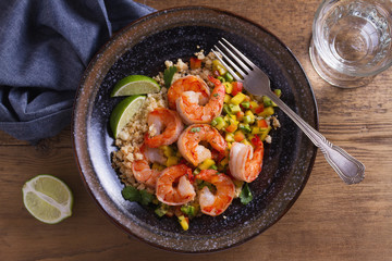Shrimps with mango avocado and red pepper salsa on cauliflower rice in bowl on wooden table. View from above, top studio shot