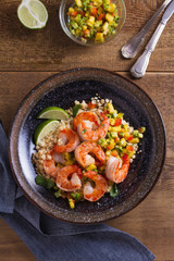 Shrimps with mango avocado and red pepper salsa on cauliflower rice in bowl on wooden table. View from above, top studio shot