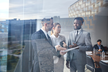 Three elegant colleagues discussing main points of report or paper in conference hall before event