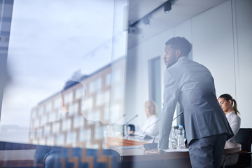 Young African-american businessman bending over table with microphone while listening to colleague...