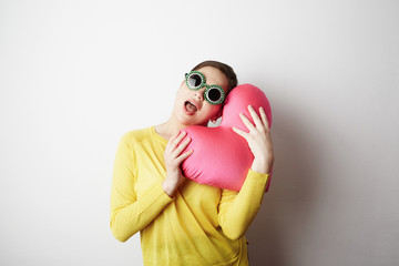 Young handsome woman in yellow tshirt holding big plush red heart over empty white background.Lifestyle and Holiday Concept