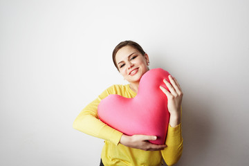 Young beautiful girl in yellow tshirt holding big plush red heart over empty white background.Lifestyle and Holiday Concept