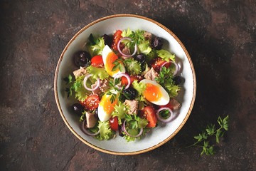 Healthy organic lettuce salad with canned tuna, cherry tomatoes, sun-dried olives, red onion, egg and parmesan. Top view. Copy space. 