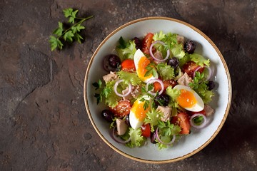Healthy organic lettuce salad with canned tuna, cherry tomatoes, sun-dried olives, red onion, egg and parmesan. Top view. Copy space. 