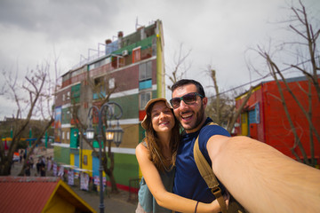 Happy tourist couple taking selfie in the Caminito, the colorful street museum in La Boca barrio,...