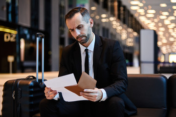 Serious business traveler reading document while sitting in airport lounge and waiting for flight