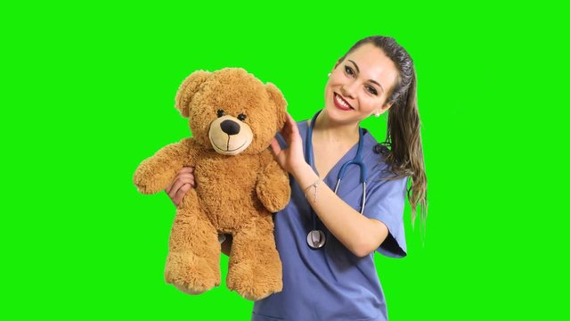 Beautiful nurse holding a teddy bear, pediatrician concept, isolated on green screen chroma key