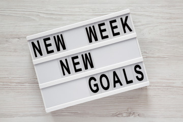 Modern board with text 'New week new goals' over white wooden background, top view. From above, flat lay, overhead.