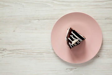 Top view, piece of homemade chocolate cherry cake on a pink plate over white wooden surface. Flat lay, from above, overhead. Copy space.
