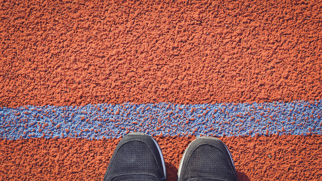 Feet in sneakers standing in front of the tracking field line. Top view