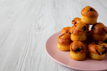 Homemade muffins with cherry on pink plate over white wooden background, side view.