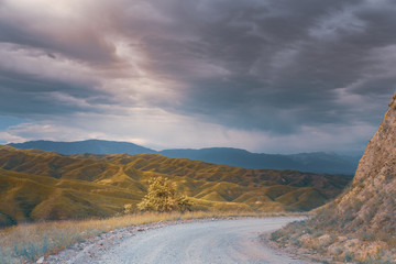 Road to the mountains. A ray of sunshine through the clouds. Beautiful sunset landscape in the mountains.