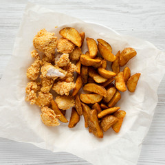 Fried potato wedges and chicken bites on a white wooden background, top view. Flat lay, overhead, from above.