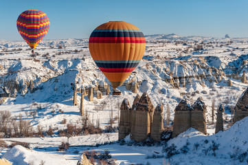 colorful balloon over the extraordinary rocks formations rock hills on snowy winter of Cappadocia,...