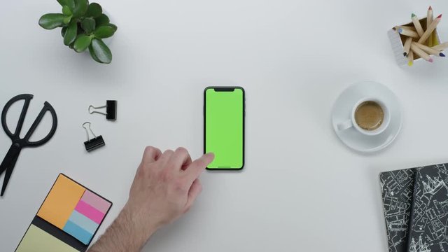 Male hands using smart device with green screen chroma on white clean minimalistic table with top view