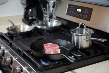 New York strip steak cooking in a cast iron pan on a natural gas stove top.