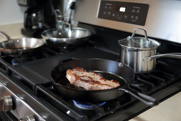 New York strip steak frying in a cast iron pan on a natural gas stove top.
