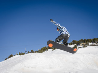 Jumping snowboarder with a blue and sunny sky in Zermatt, the swiss Alps