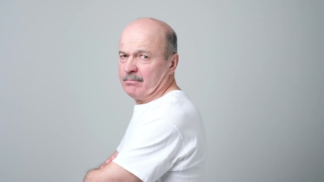 Senior man stands with his back to the camera and turns looking irritated