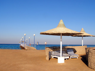 Sandy beach with umbrellas, sun loungers and a pier in Egypt coast.