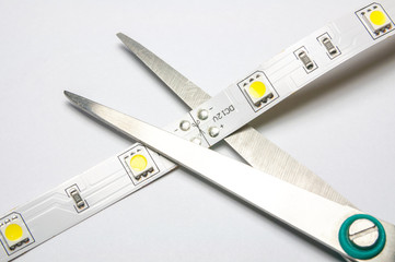 Pair of scissors cut the LED tape on white background. Scissors near the designated area for the cut.