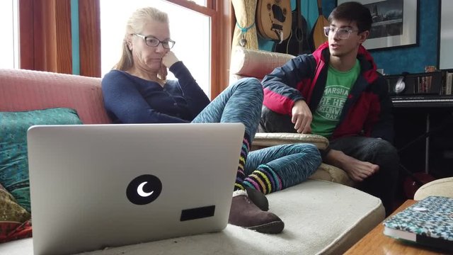 Teen son talks to his mature mother while his mother looks disparagingly at a computer screen.
