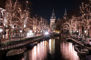 Fototapeta na wymiar AMSTERDAM, NETHERLANDS - DECEMBER 12, 2018: illuminated trees and buildings reflected in water at Spiegelgracht Amsterdam in december by night