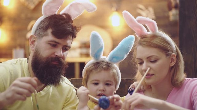 Close-up of happy family which are painting easter eggs. Cute little child boy wearing bunny ears. mother, father and their son painting Easter eggs. Easter eggs on wooden background.