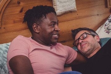 An interracial gay couple talking, lying down in their bedroom. 