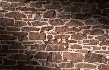Old masonry wall using irregular stones lit diagonally
