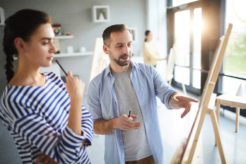 Fototapeta premium Confident teacher of painting pointing at sketch of young student while explaining what could be changed